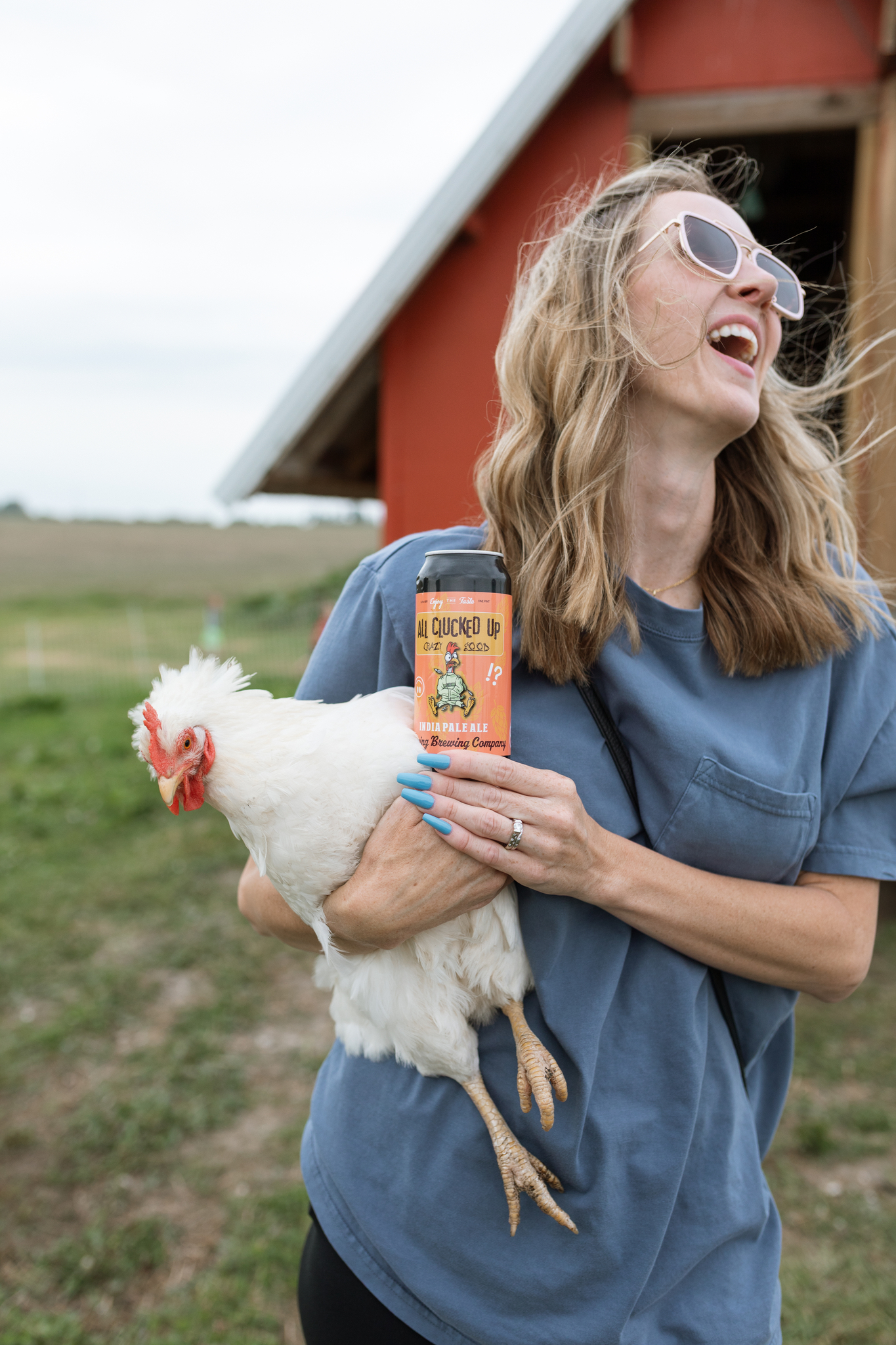Laughing woman holding a chicken and a can of All Clucked Up at the coop