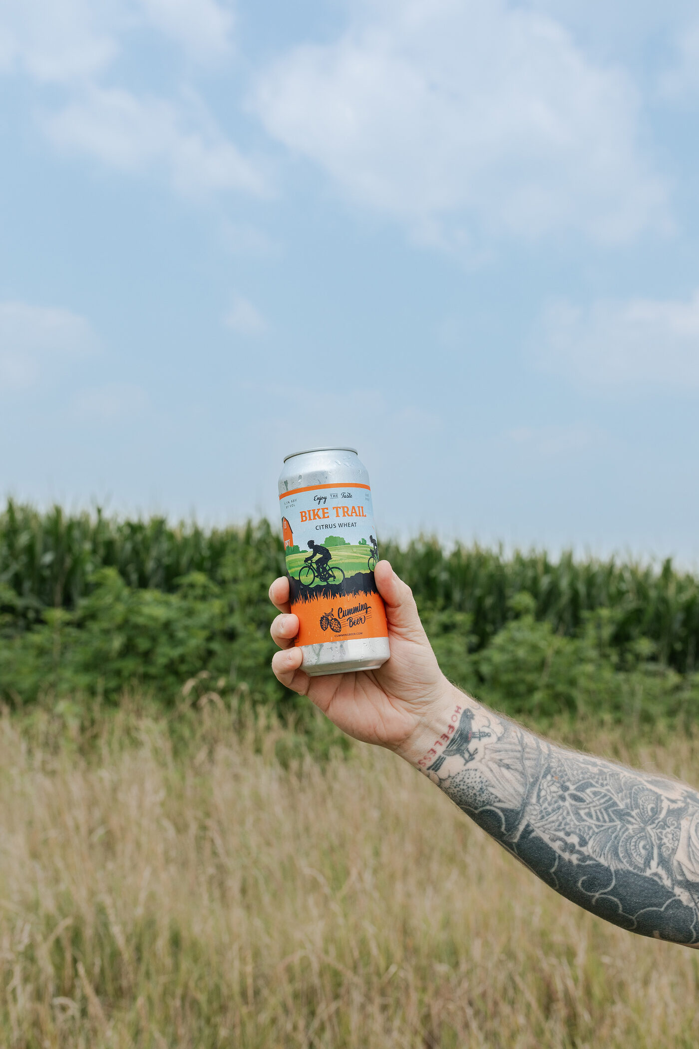 Holding a can of Bike Trail Citrus Wheat up against an Iowa cornfield